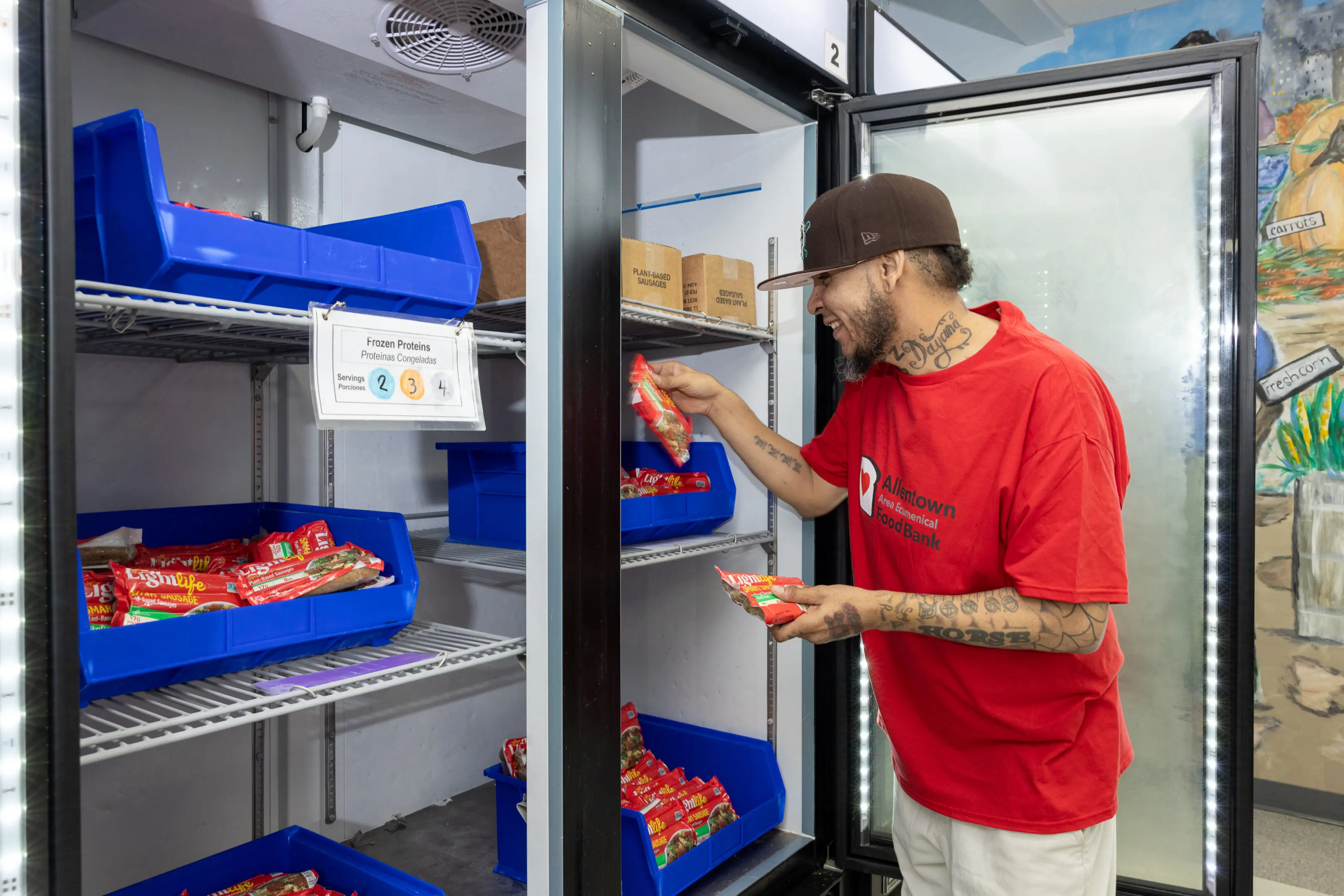 OUR TEAM - HERO A man in red shirt standing next to refrigerator.