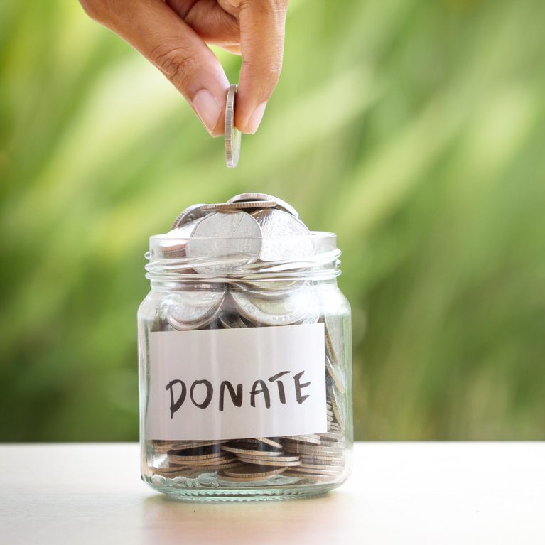 Hand putting Coins in glass jar for giving and donation concept