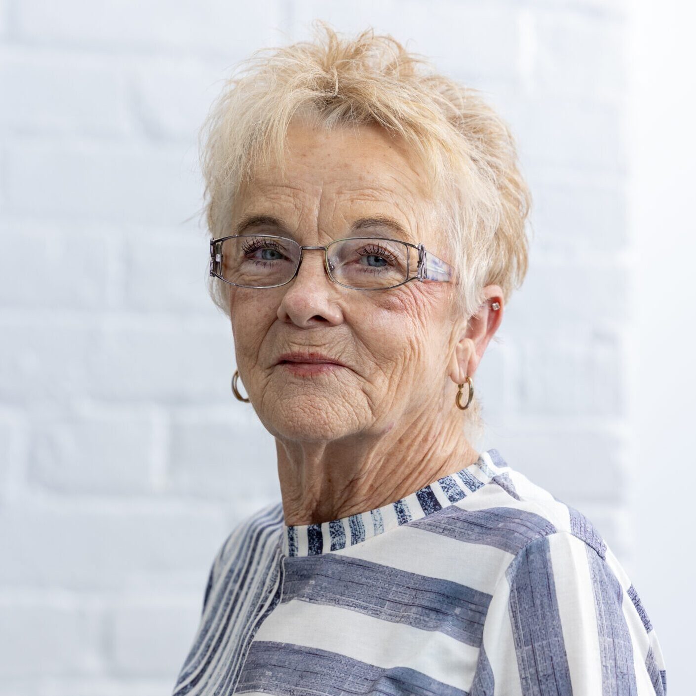 OUR TEAM - Donna(1) A woman with short blonde hair wearing glasses.
