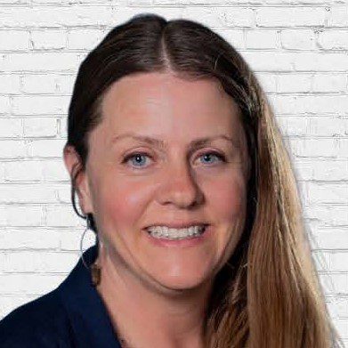 OUR TEAM - Nicole Shelly Headshot A woman with long hair is smiling for the camera.